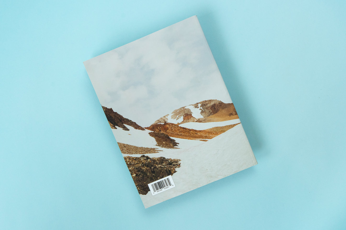 The back of a magazine is over a blue background. The image is a bright snowy mountain scene with peeks of muted yellow and orange tone rocks peeking out of the snow covered ground.