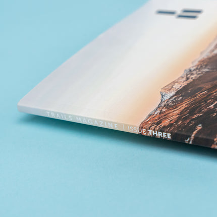 The binding of a magazine, displaying a mountain ridge that is illuminated in reds and oranges from the sunrise. The text along the binding reads, "Trails Magazine Issue Three".