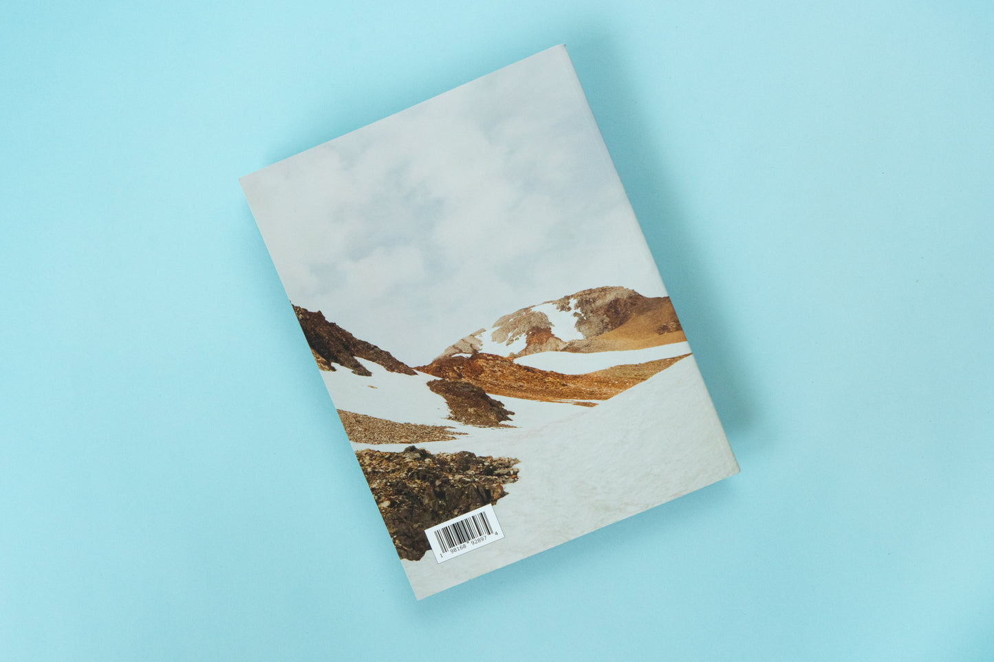 The back of a magazine is over a blue background. The image is a bright snowy mountain scene with peeks of muted yellow and orange tone rocks peeking out of the snow covered ground. 