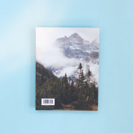 The back of a magazine is over a blue background. The image is a cold and foggy mountain scene with peaks peering out of the fog and pine trees in the foreground.