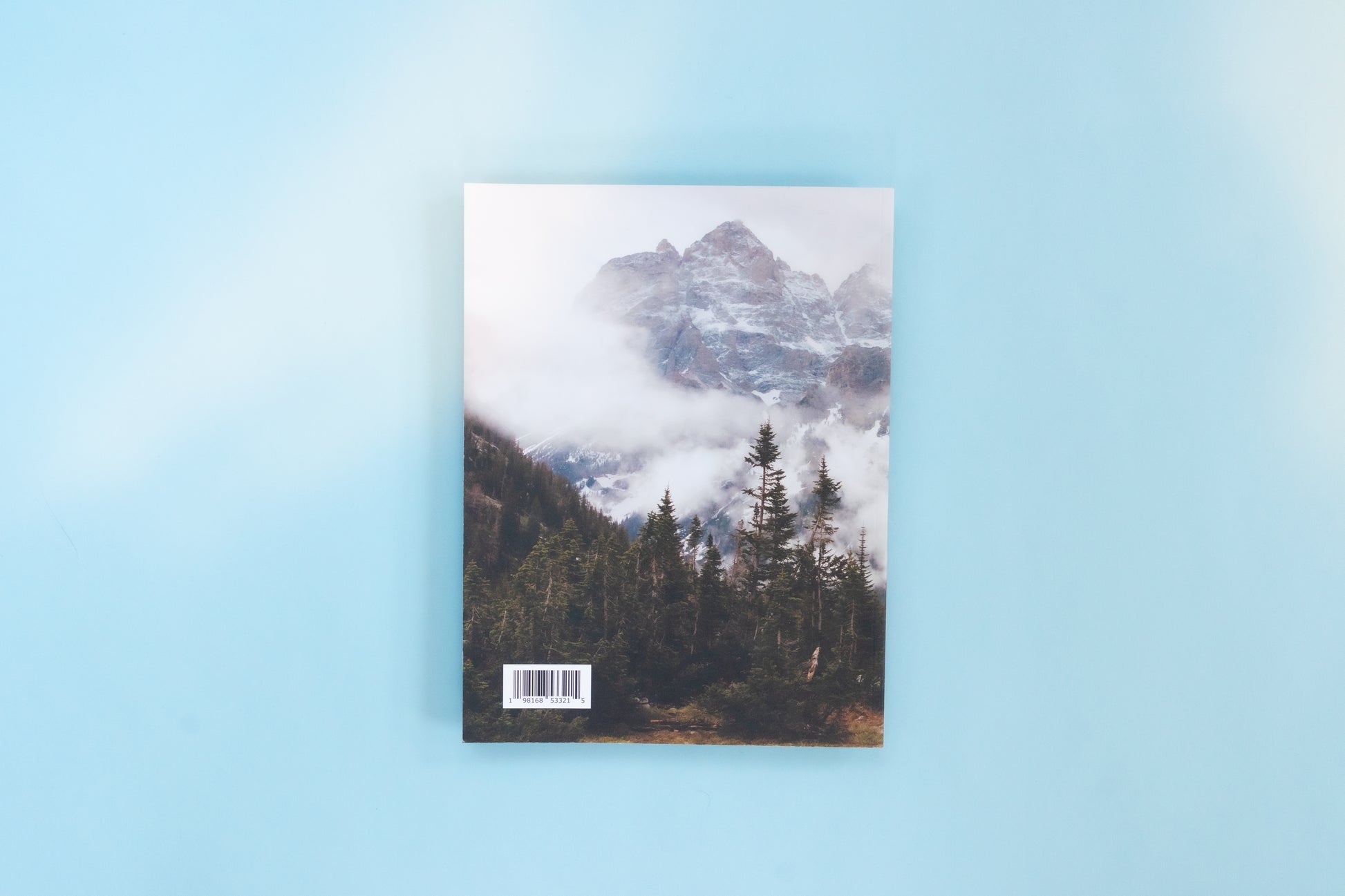 The back of a magazine is over a blue background. The image is a cold and foggy mountain scene with peaks peering out of the fog and pine trees in the foreground.