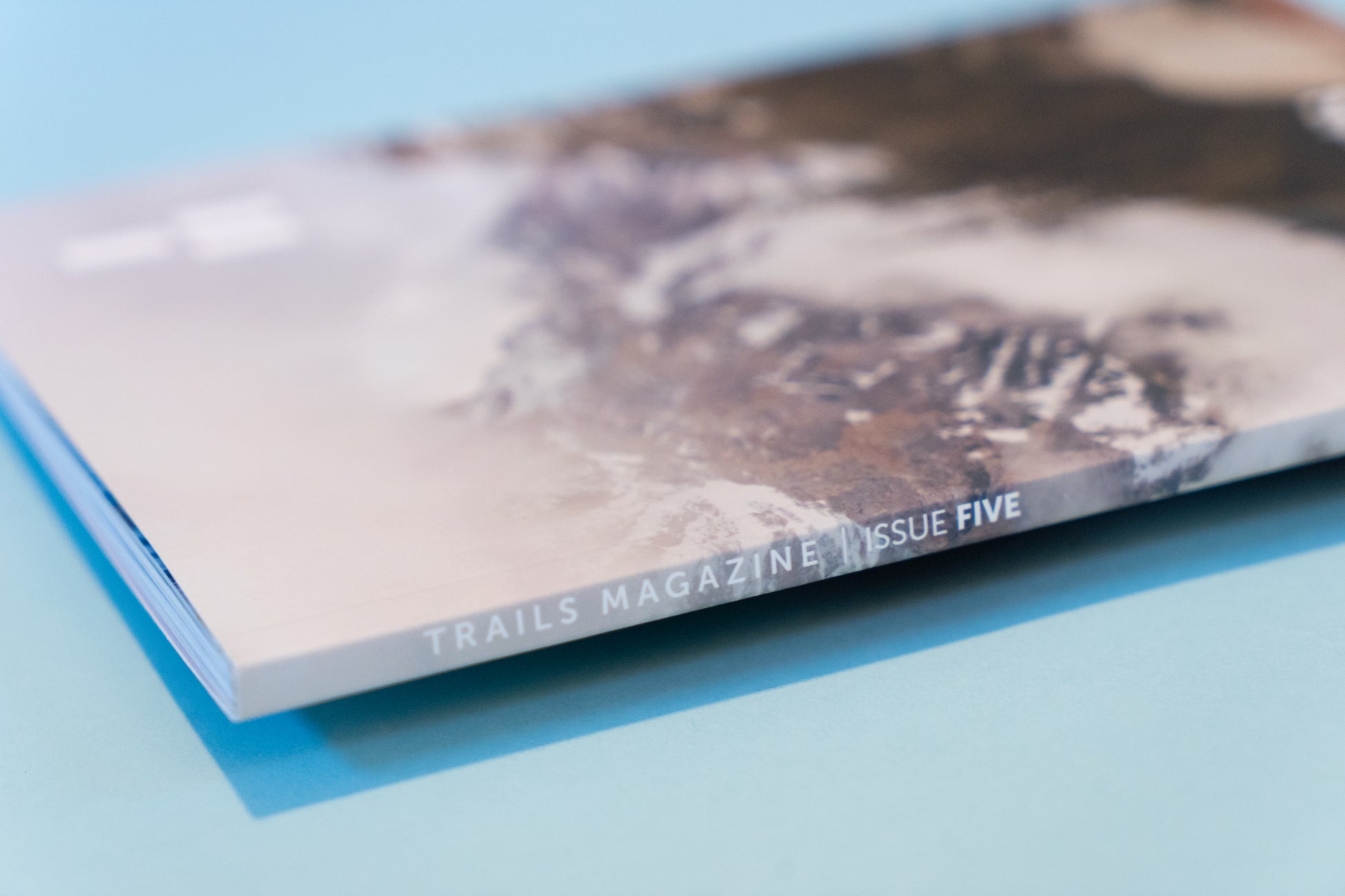 The binding of a magazine, displaying a mountain scene lays across a light blue backdrop. The text along the binding reads, "Trails Magazine Issue 5"